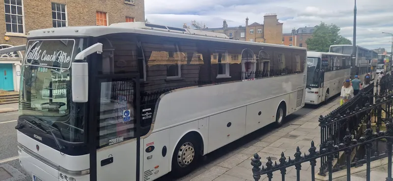 White coach parked alongside a roadside fence
