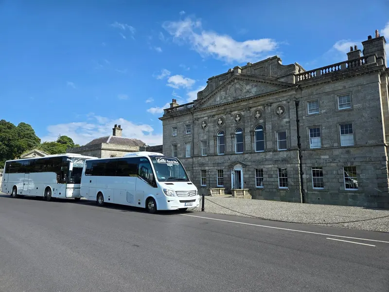 Coach and mini coach parked beside a historic stone building